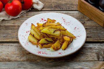 fried potatoes with onions on plate on old wooden table side view