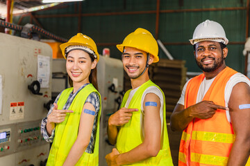 Asian young workers and African man pointing at his arm with a bandage after receiving the covid-19 vaccine.Vaccination for Essential Workers in healthcare at industrial factory.
