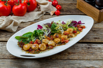 grilled scallop with greens and vegetables on white plate on old wooden table
