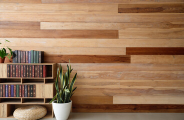 Stylish bookcase with houseplants and pouf near wooden wall