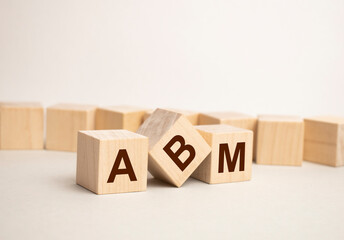 On a white damaged wood board, wooden word cubes are arranged in the letters ABM. It is an abbreviation for Account Based Marketing.