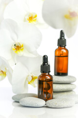 Beauty and aromatherapy.Massage oil and massage stones.glass bottle with oil on gray stones and white orchid flower on white background.Spa and relaxation