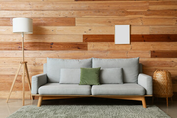 Comfortable sofa, floor lamp and blank photo frame on wooden wall in room interior
