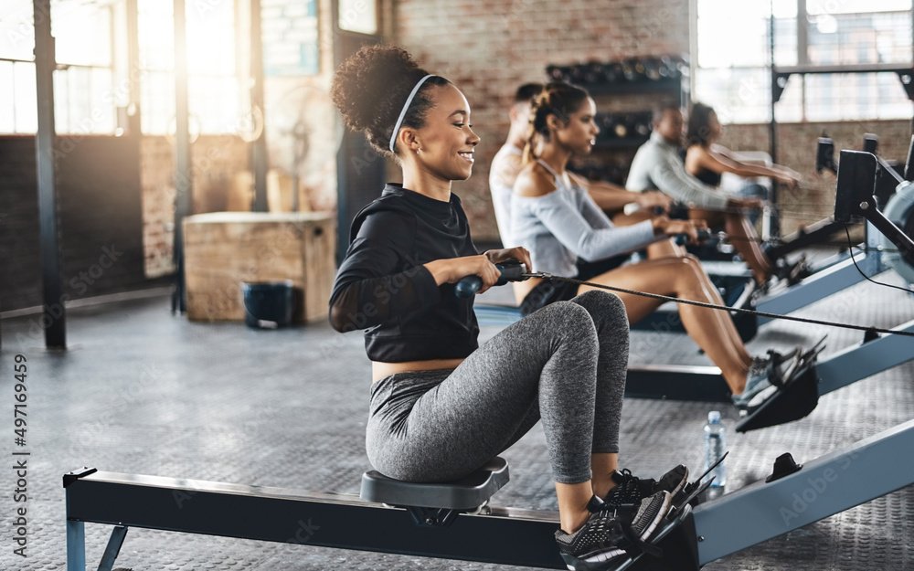 Poster working out like a pro. shot of a young woman working out with a rowing machine in the gym.