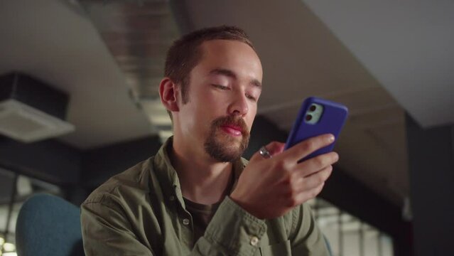 A young man-student sits on the chair and reads humorous posts on the Internet, close up