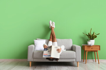 African-American teenage girl with magazine relaxing on sofa at home