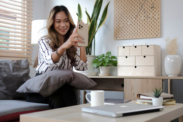 Happy millennial female having video call on smartphone while sitting on couch at home. Communication concept.