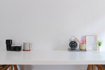 Creative workplace with camera, coffee cup, stationery and picture frame on white table.