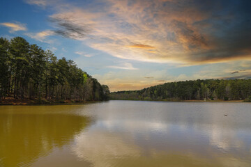 Fototapeta na wymiar a stunning shot of the vast still waters of a lake surrounded by lush green trees with powerful clouds at sunset at Murphey Candler Park in Atlanta Georgia USA 