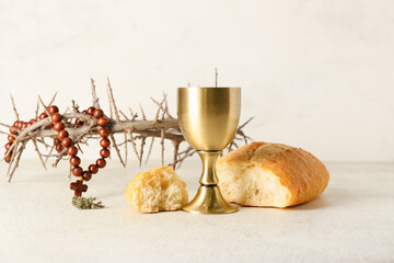 Cup of wine with bread, crown of thorns and rosary on light background