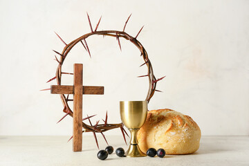 Cup of wine with bread, cross and crown of thorns on light background