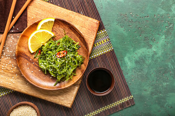 Plate with healthy seaweed salad, lemon and sauce on green background