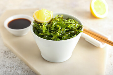 Bowl with healthy seaweed salad, lemon and sauce on light background