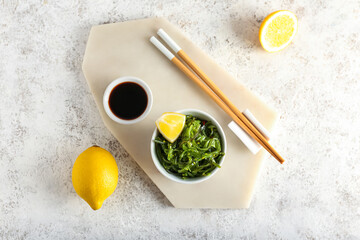 Bowl with healthy seaweed salad, lemon and sauce on light background