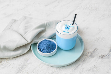 Glass of blue matcha tea and bowl with powder on light background