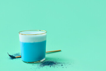 Glass of blue matcha tea and chashaku with powder on turquoise background