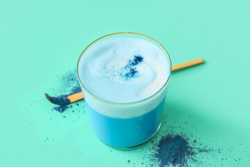 Glass of blue matcha tea and chashaku with powder on turquoise background