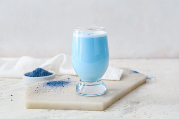 Glass of blue matcha tea and bowl with powder on light background