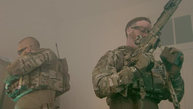 Concentrated soldiers in bulletproof vests testing rifles. Medium shot of focused men in camouflage uniform preparing for shooting, loading guns. Military, security, attack concept