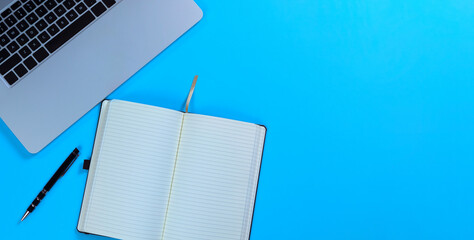 Blue desktop with writing paper, pen, and laptop computer