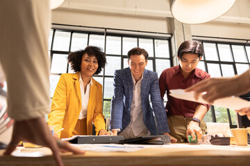 A cheerful young business team, Caucasian and Asian, man and women standing around table, brainstorming about work on table.. Meeting of business partners at the conference on business development
