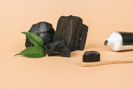 Whitening toothpaste with charcoal, green leaves and pieces of charcoal on a beige background.