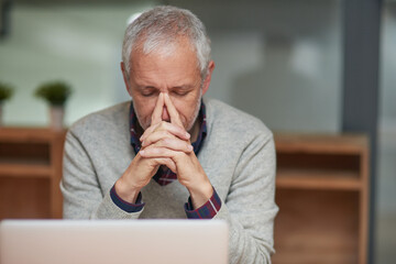 Fototapeta premium The pressure is getting to him. Shot of a stressed out mature businessman using a laptop while working in an office.