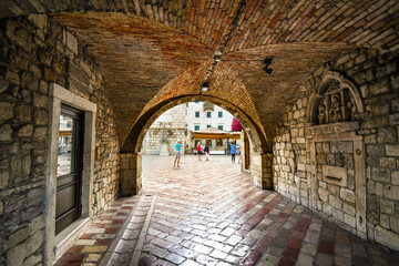 The Square of the Arms opens out  in front as tourists enter the gated, walled medieval fortress town of Kotor, Montenegro through it's tunnel entrance.