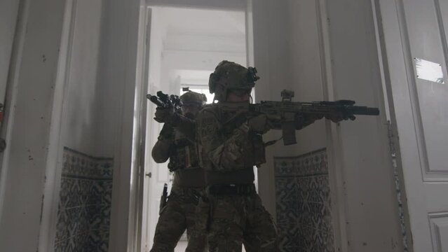 Men with guns in camouflage uniform walking down hall. Front view of concentrated male friends storming building, taking sight, playing airsoft in building. Physical activity, airsoft game concept