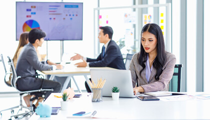 Asian young pretty thoughtful concentrated female professional successful businesswoman in formal business suit sitting holding pen at chin thinking about customer job task solution ideas with laptop