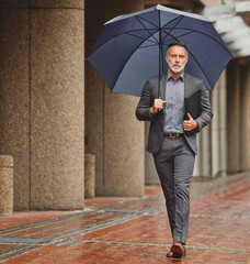 Making my way downtown to work. Shot of a handsome businessman walking to work on a rainy day.
