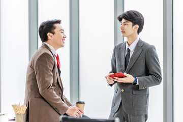 Asian male professional businessmen colleague in formal business suit take coffee break standing holding disposable paper cup and tablet computer talking have conversation together in front monitor