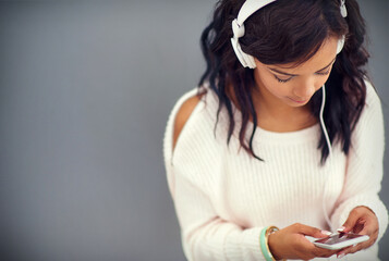 Fototapeta premium She never misses an episode of her favorite podcast. Studio shot of a young woman listening to music while using her phone against a gray background.