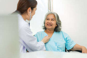 Physician examining heart with a stethoscope and talking with a senior woman at a clinic for check...