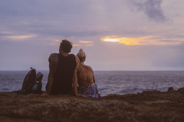 A young couple in love on a journey sits on the edge of a cliff and watches the sunset.