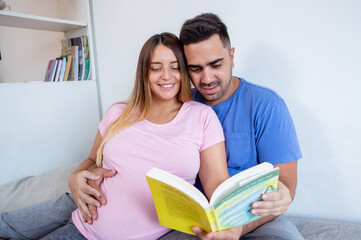 portrait of pregnant couple sitting on bed reading together