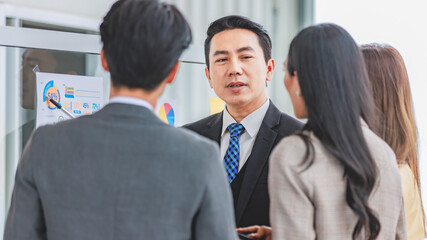 Asian happy male and female professional successful businessman and businesswoman colleagues partnership teamwork in formal business suit standing smiling look at post it note on glass board together