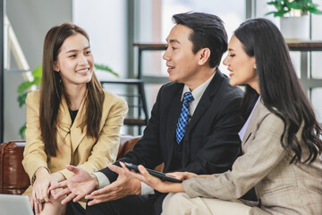 Group of millennial Asian young happy male female businessman businesswoman employee staff in formal business suit sitting on leather sofa smiling discussing brainstorming talking together in office