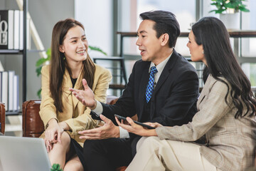 Group of millennial Asian young happy male female businessman businesswoman employee staff in formal business suit sitting on leather sofa smiling discussing brainstorming talking together in office