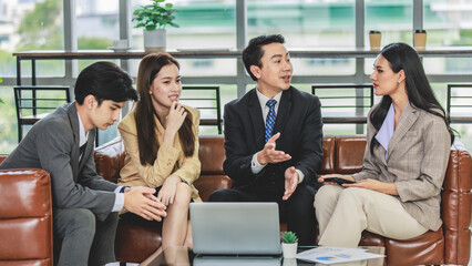 Group of millennial Asian young happy male female businessman businesswoman employee staff in formal business suit sitting on leather sofa smiling discussing brainstorming talking together in office