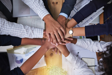 Were all in this together. High angle shot of a group of businesspeople putting their hands in a pile in the office.