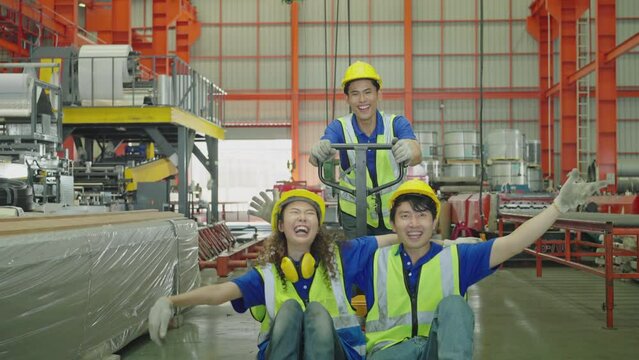 Factory workers are happy and enjoying themselves on a hand pallet truck. Young Asian men push hand pallet stacker. Women raise their arms into the air while open arms enjoy colleagues. Slow Motion