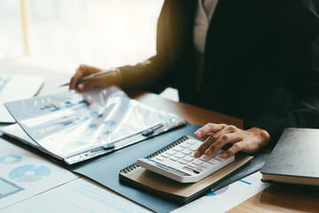 Young businessman using calculator and laptop computer is now finalizing sales this year to analyze...