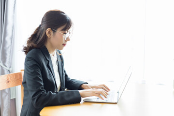 A Southeast Asian woman wearing a suit and typing documents on her laptop computer.