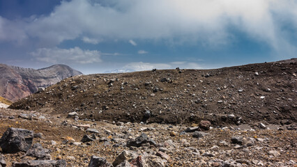 The soil at the top of an active volcano is strewn with rocks. The edge of the crater and the layered structure of the slope against a background of blue sky and clouds. Kamchatka. Gorely Volcano © Вера 