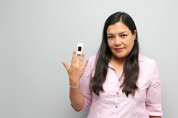 Latin adult woman with dark brown hair shows in her hand an oximeter on her finger that measures her oxygenation for suspicion of Covid-19 in the new normality due to the coronavirus pandemic
