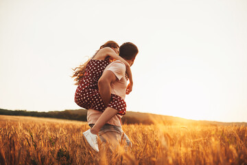 Handsome man giving piggy back to his girlfriend on a sunny day in the wheat field. Beautiful young...