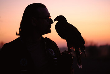 Silhouette of man and wild bird over sunset sky looking on each other Buzzard or eagle symbol of...