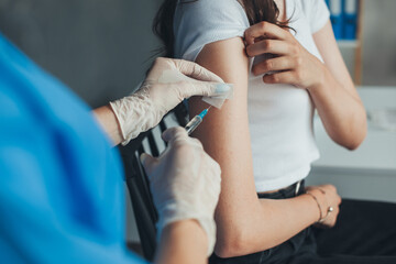 Doctor wearing white gloves giving COVID -19 coronavirus vaccine injection to a woman's arm in...