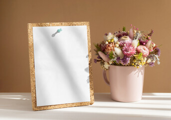 Delicate bouquet of flowers in pink vase next to empty notebook, calendar-glider on wooden surface. Close-up, white-beige background with striped shadow. Ready-made mockup for advertising, ads